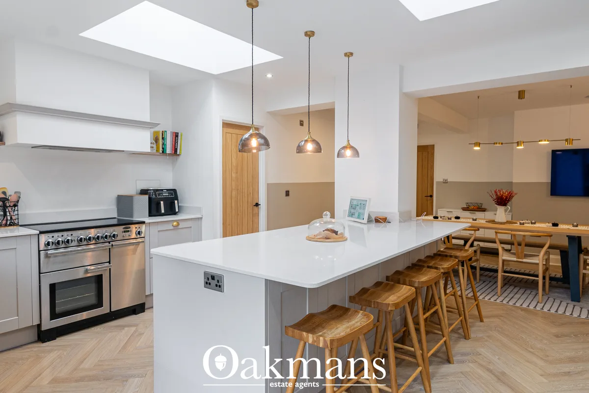 Modern open-plan kitchen with white cabinetry, stainless steel range cooker, white island with wooden bar stools, pendan
