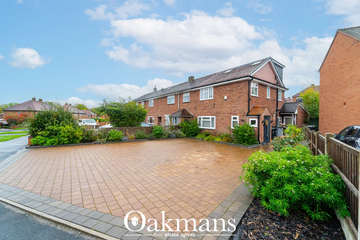 Brick semi-detached house with paved driveway, front garden landscaping, and clear blue sky