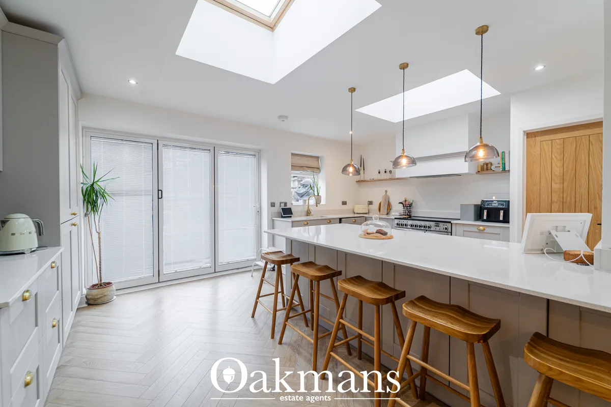 Modern fitted kitchen with white cabinetry, white worktops, island with wooden bar stools, pendant lights, skylights and