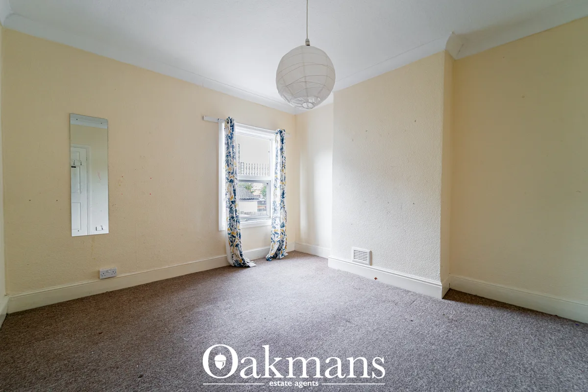 Spacious living room with cream walls, grey carpet, pendant light, window with blue floral curtains and wall mirror