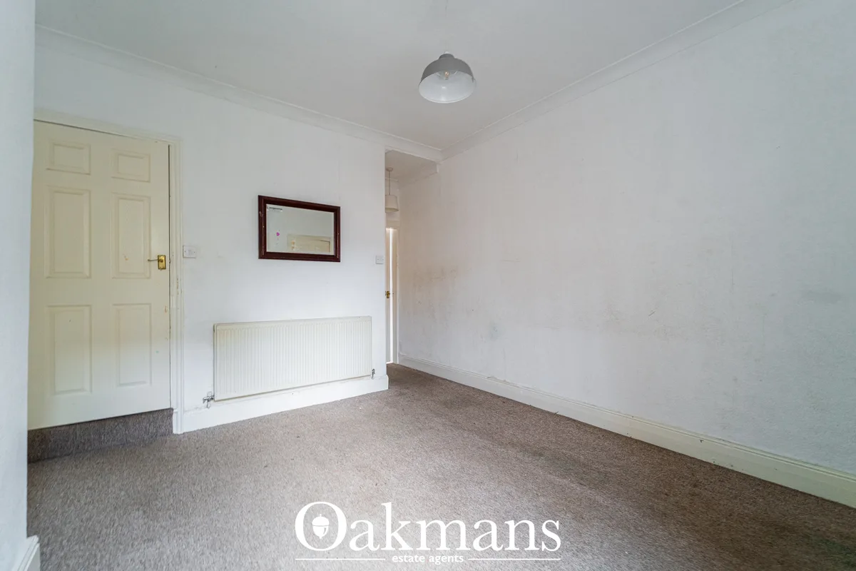 Bright hallway with cream six-panel door, white walls, radiator, framed mirror, ceiling light and beige carpet