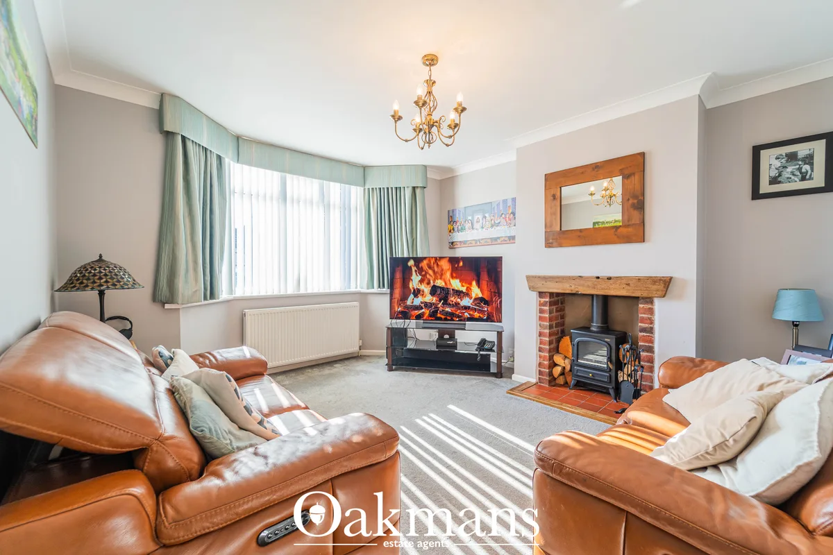 Spacious living room with two tan leather sofas, fireplace with wood stove, TV on stand, bay window with pale green curt