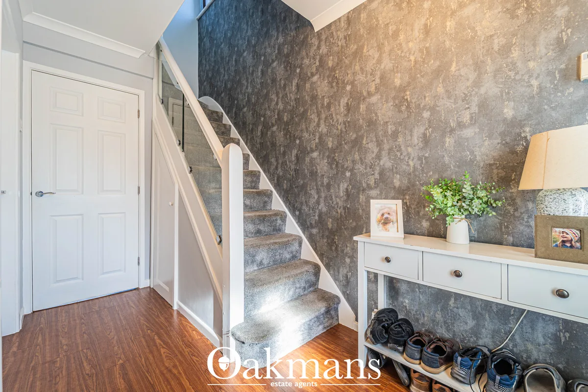 Bright entrance hallway with dark textured wallpaper, wooden flooring, white door, staircase with grey treads, white pai