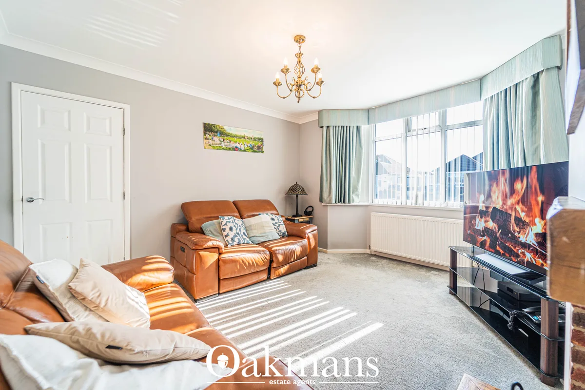 Spacious living room with tan leather sofas, fireplace on TV, bay windows with pale blue curtains, cream ceiling with go