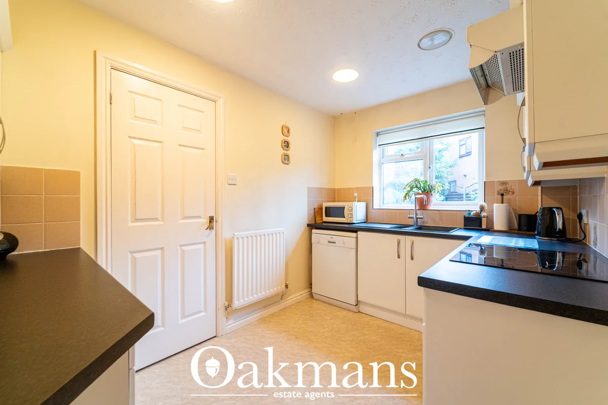Bright kitchen with cream units, black worktops, window overlooking street, recessed lighting, radiator and tiled splash
