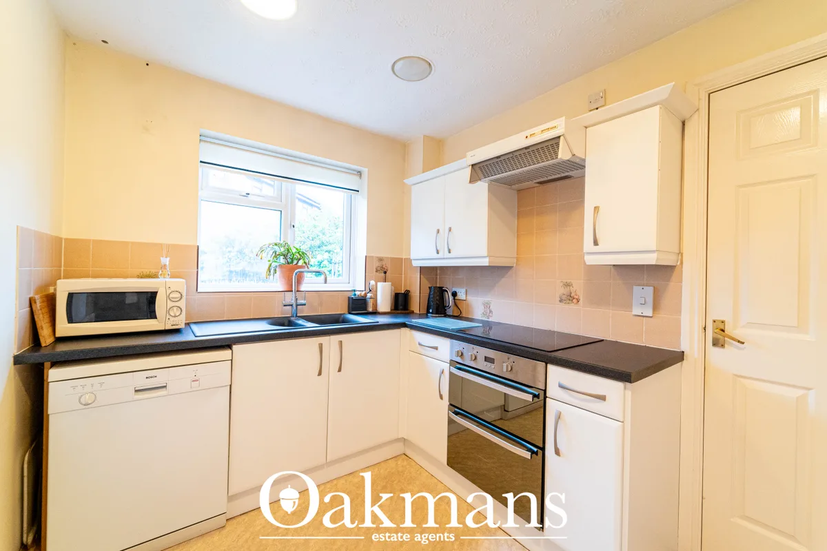 Fitted kitchen with cream units, black worktops, integrated appliances, tiled splashback and window overlooking garden