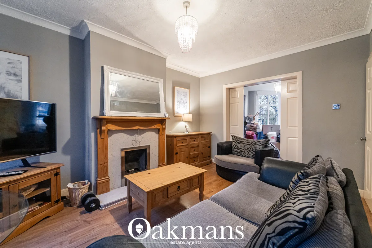Spacious living room with fireplace, wood furnishings, grey upholstered sofa with patterned cushions, TV, and cream wall