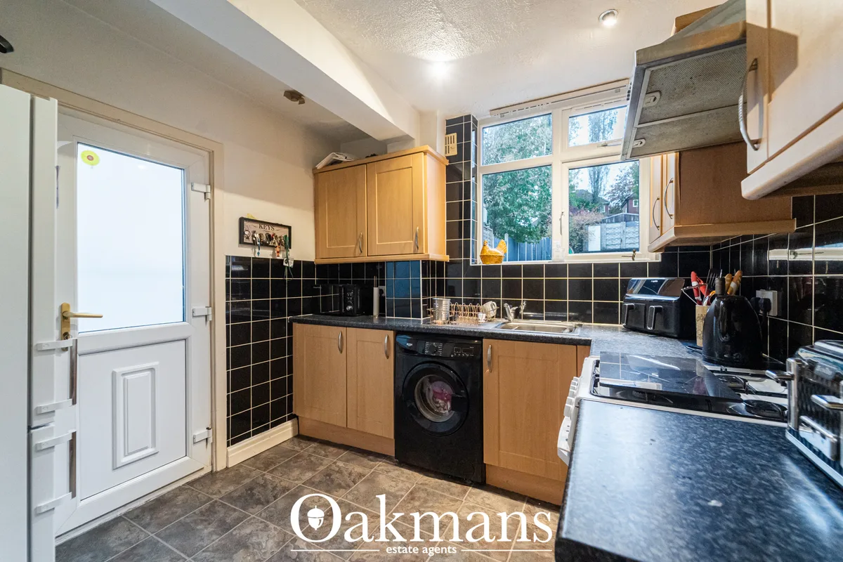 Modern fitted kitchen with wooden units, black tiled splashback, black worktops, integrated appliances and garden views 