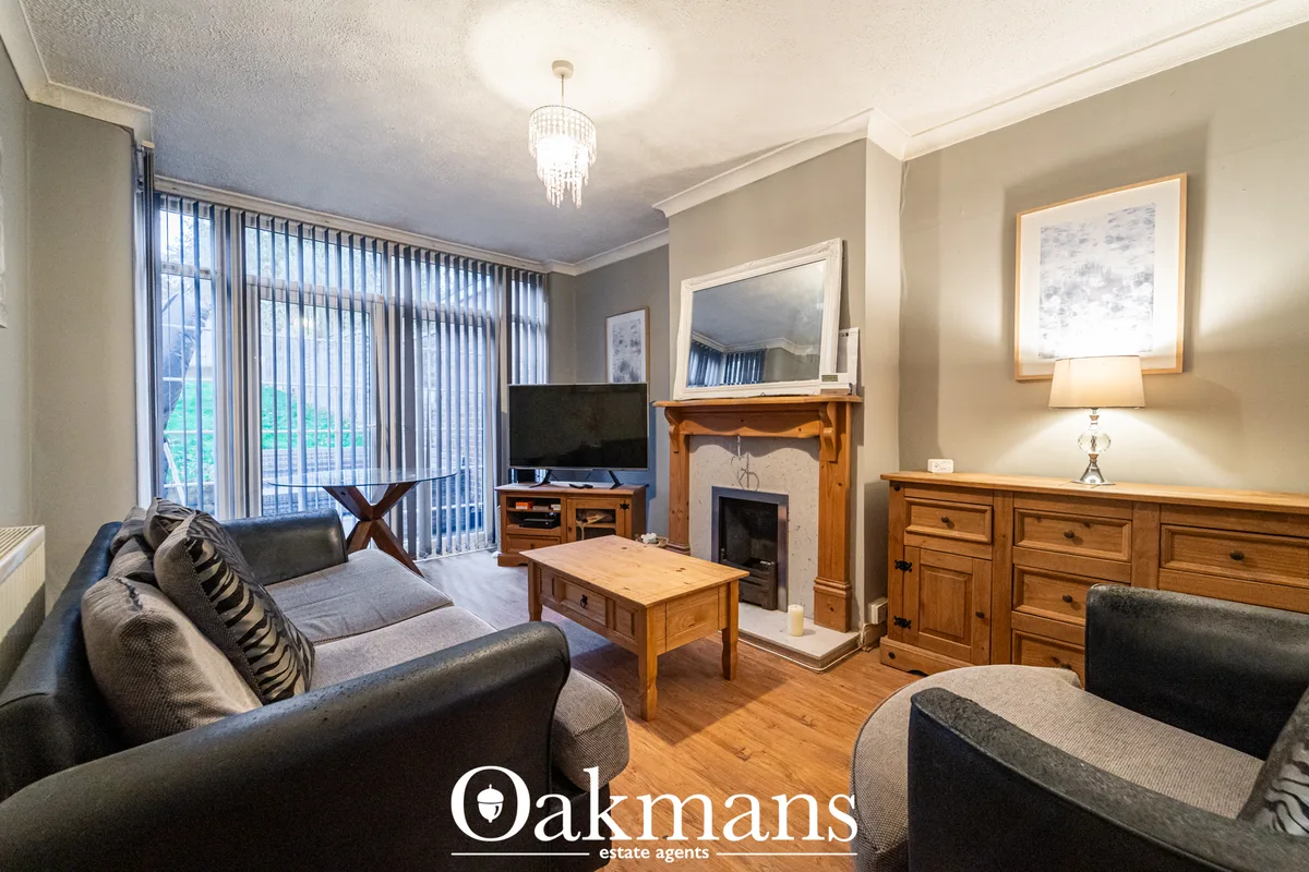 Spacious living room with dark sofas, wooden furniture, fireplace, TV, large windows with vertical blinds, wooden floori