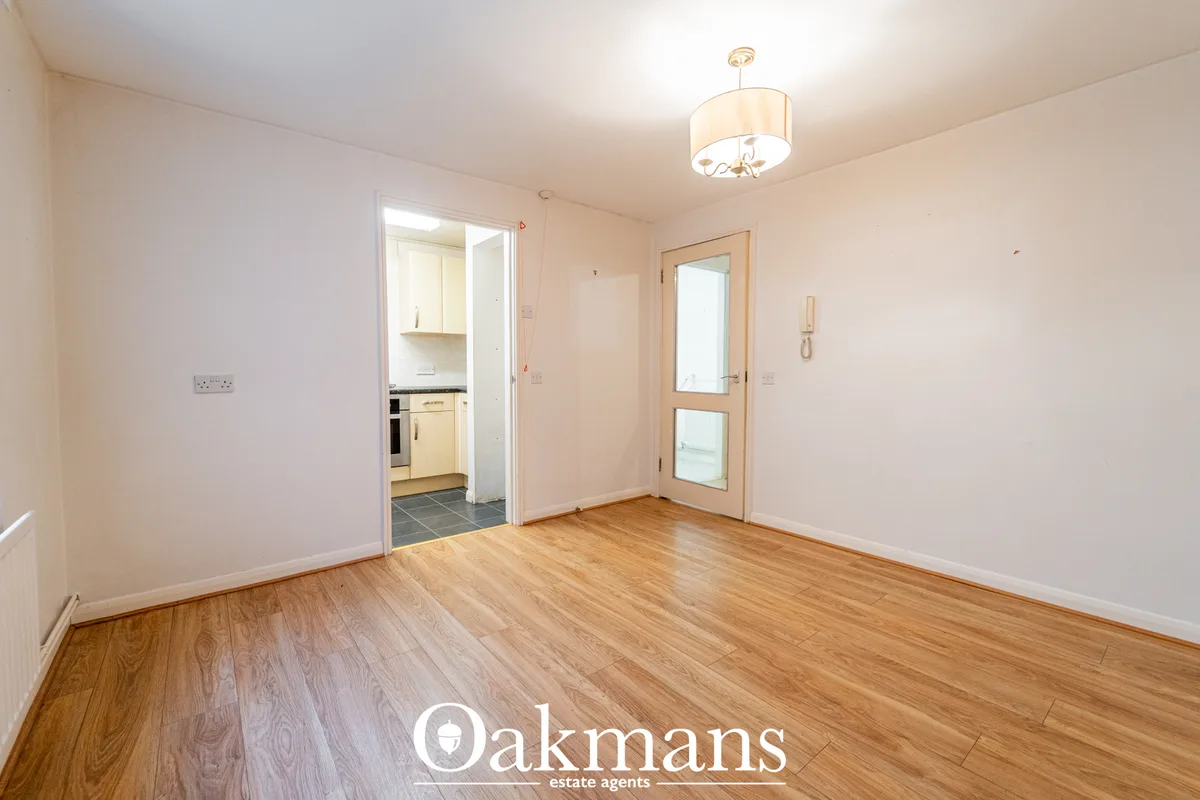 Bright living room with wooden flooring, cream walls, pendant ceiling light, open doorway to kitchen and door to exterio