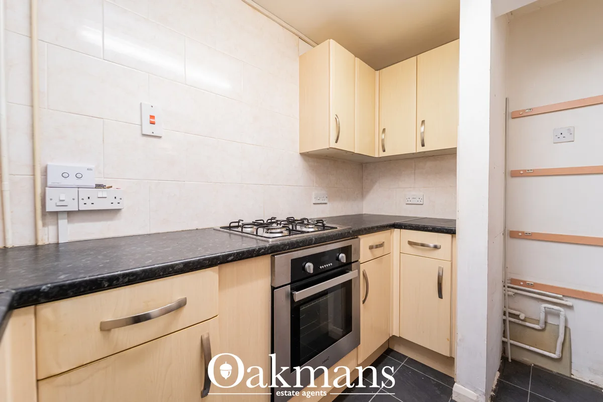 Fitted kitchen with light wood units, black granite worktops, built-in gas hob and oven, white tile splashback