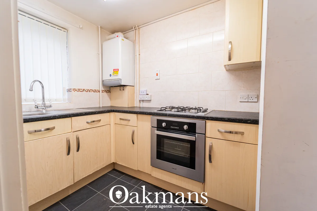 Modern fitted kitchen with light wood units, black granite worktops, integrated gas hob and oven, stainless steel sink w