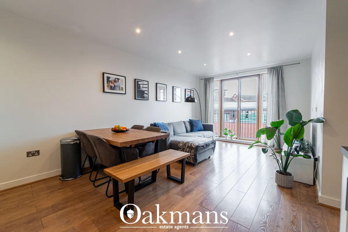Bright open-plan living and dining area with wooden flooring, grey sofa, dining table with bench seating, large windows 