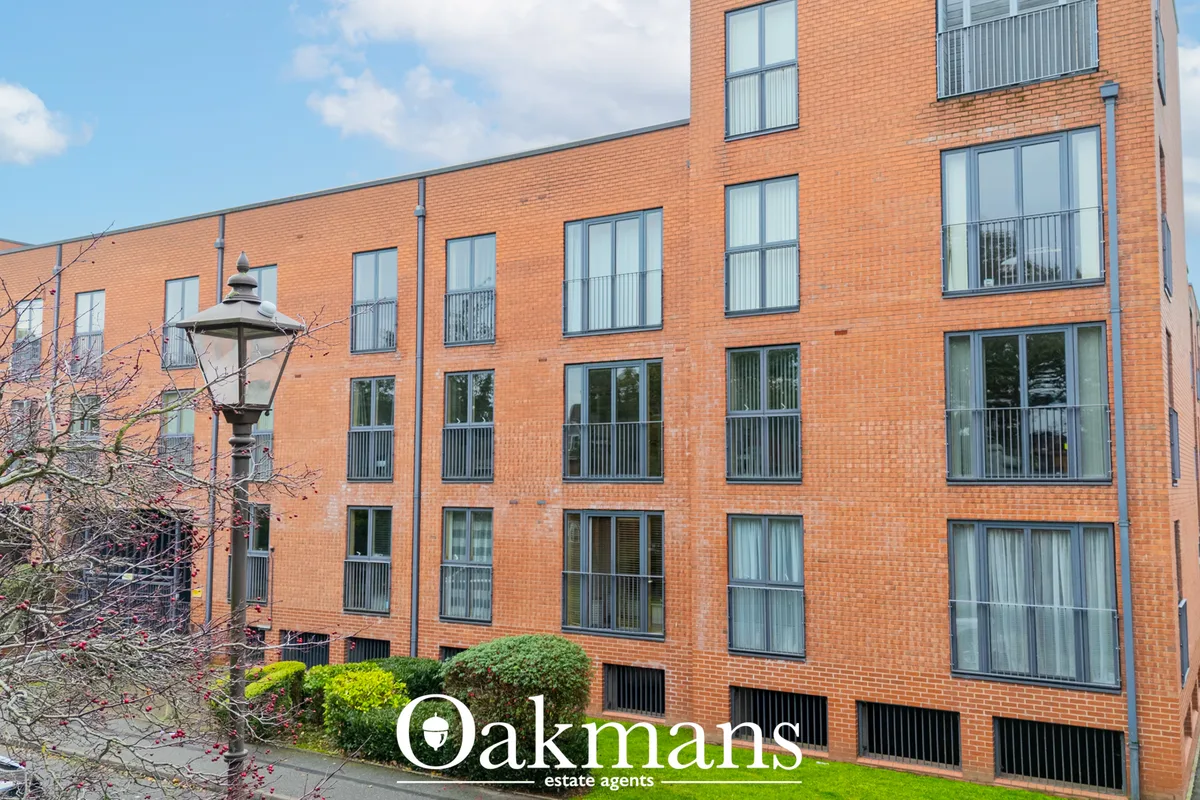 Modern red-brick residential building with multiple windows, metal balconies, and contemporary architecture set in urban