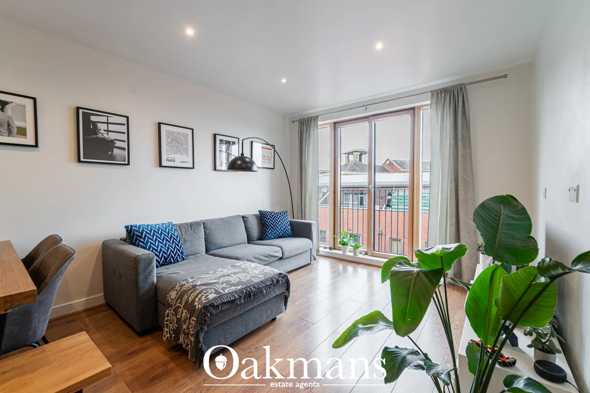 Modern living room with grey corner sofa, blue chevron cushions, wooden flooring, French doors to balcony, framed wall a