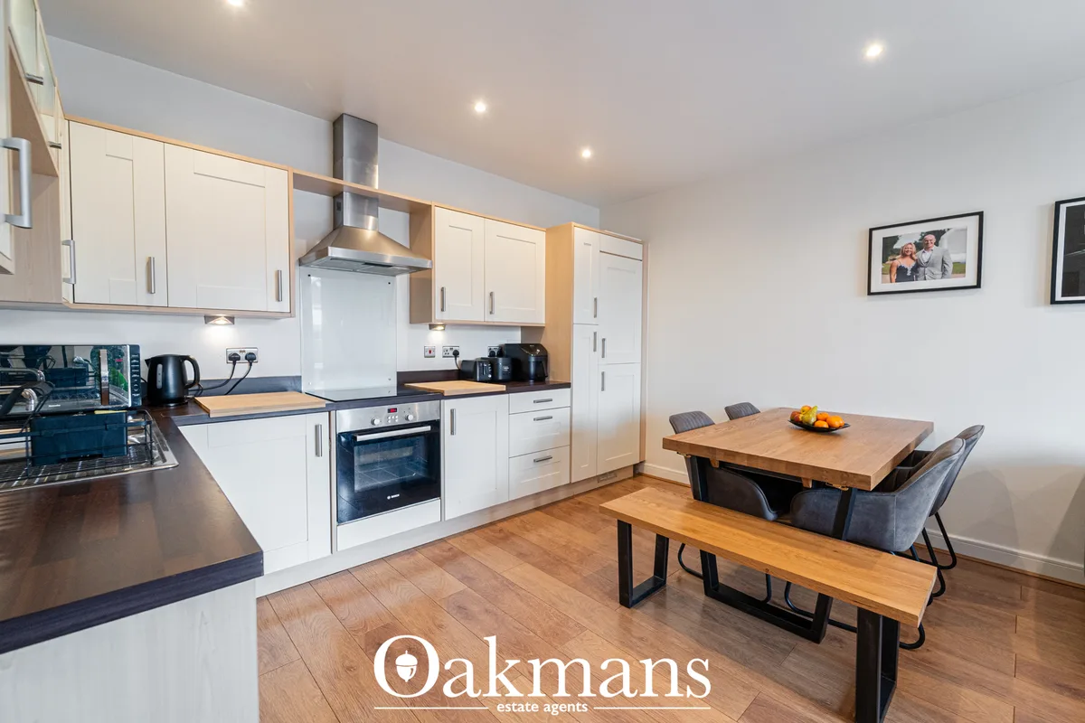 Modern open-plan kitchen with white units, wooden worktops, stainless steel range hood, and integrated dining area with 