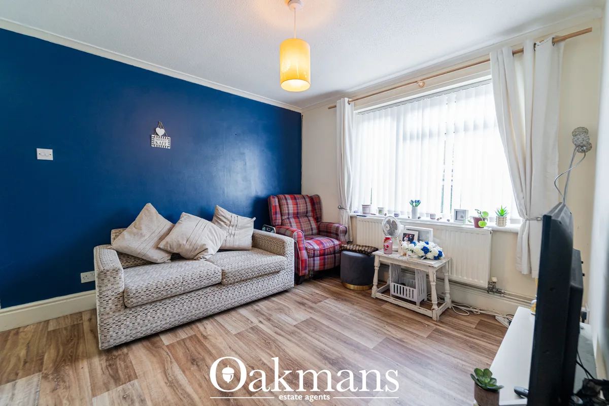 Bright living room with bold blue accent wall, beige patterned sofa, red checked armchair, wooden flooring, large window