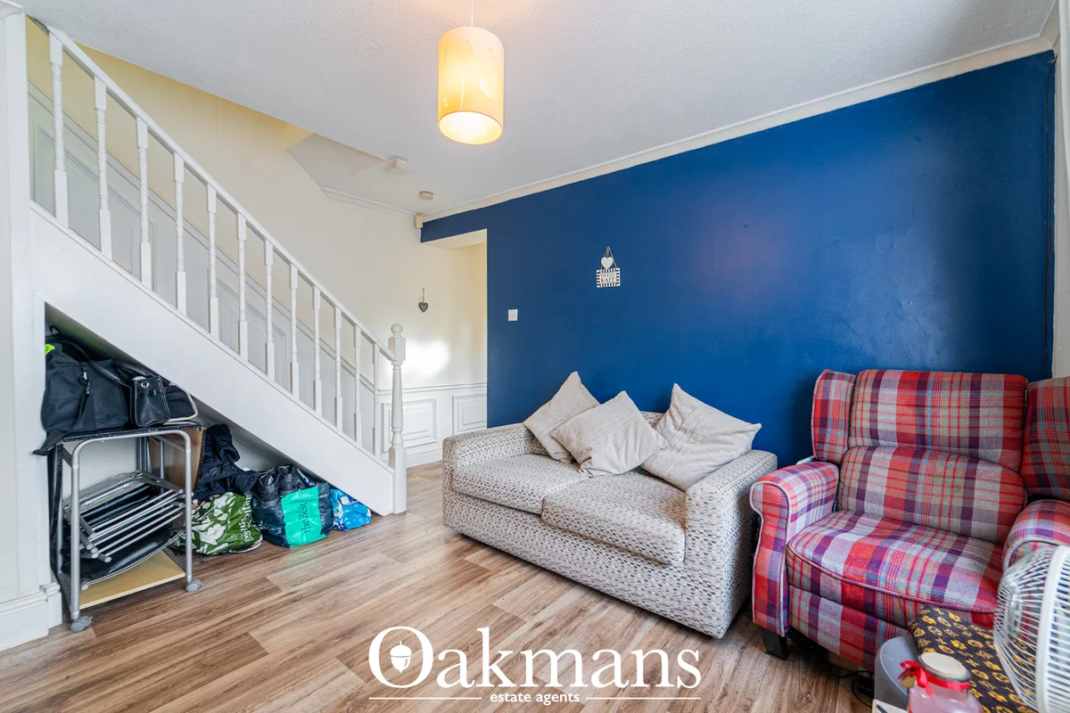 Open-plan living space with blue accent wall, beige sofa, red tartan armchair, wooden flooring, pendant lighting and mez