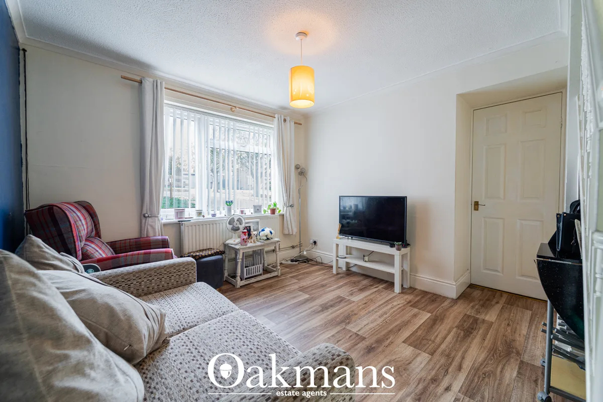 Spacious living room with cream sofas, burgundy accent chair, wooden flooring, TV on white stand, vertical blinds at win