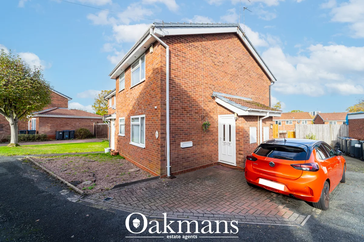 Red brick detached house with white uPVC door and window, pitched roof, brick paved driveway with orange car parked, man