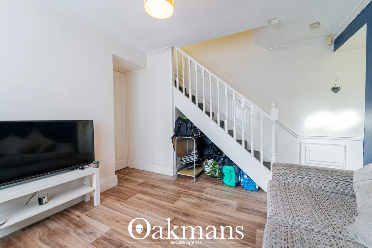 Bright living room with wooden flooring, flat-screen TV on white stand, gray upholstered sofa, white staircase with stor