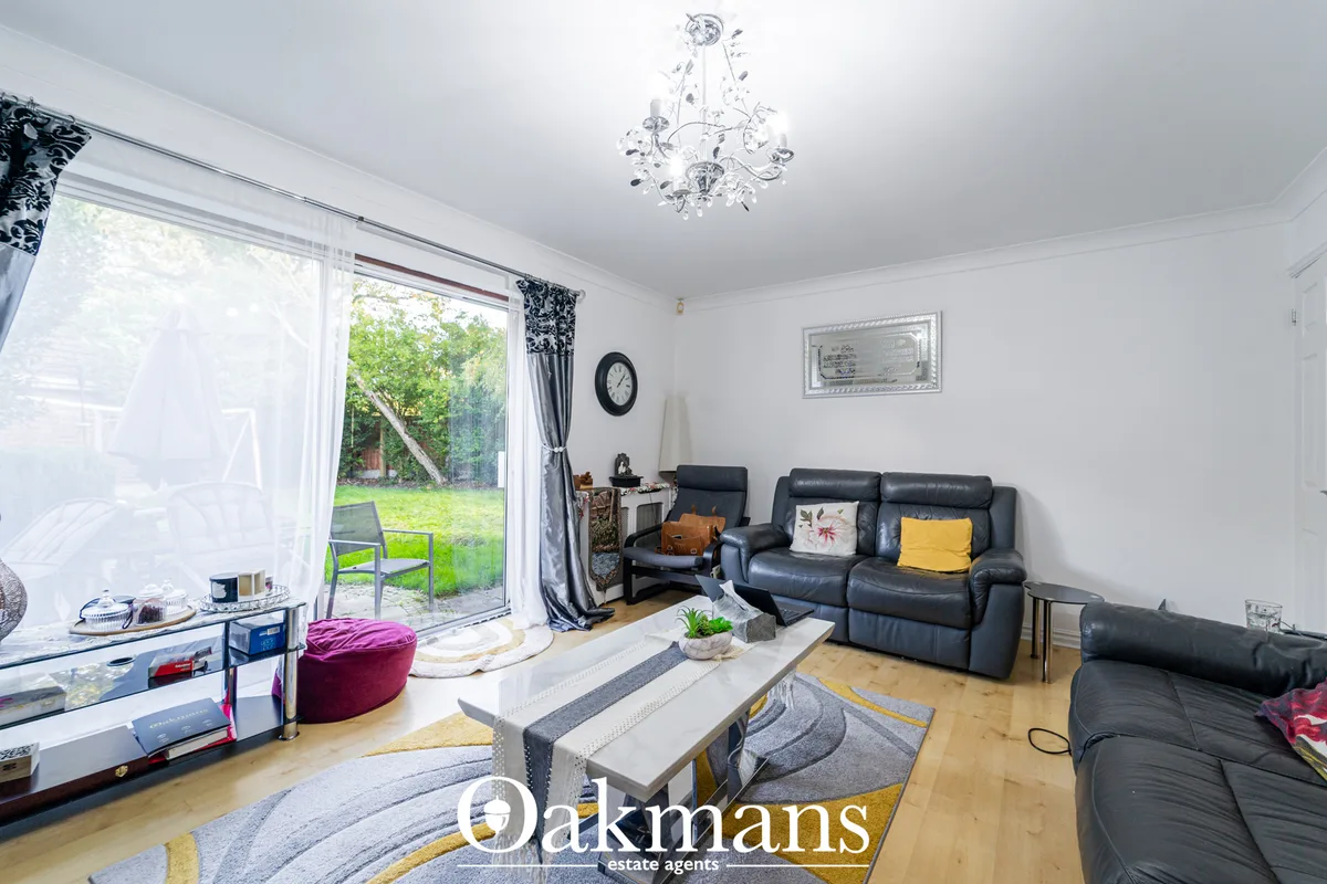 Bright living room with black leather sofas, wooden flooring, decorative chandelier, garden access via patio doors, and 
