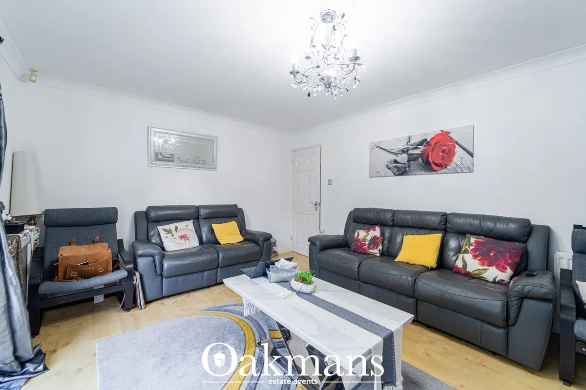 Spacious living room with dark leather sofas, white coffee table, wooden flooring, and modern ceiling light fixture