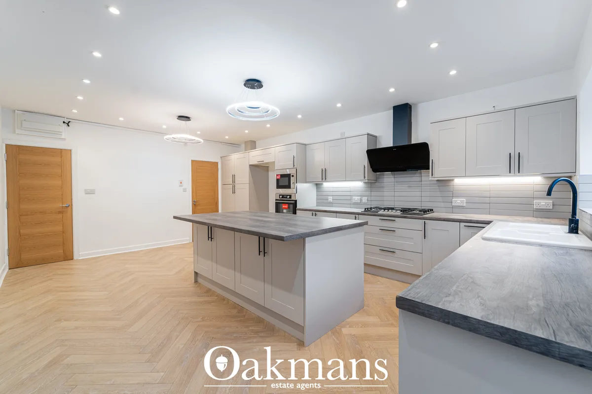 Modern fitted kitchen with white cabinetry, grey stone worktops, integrated appliances, breakfast bar island and white t
