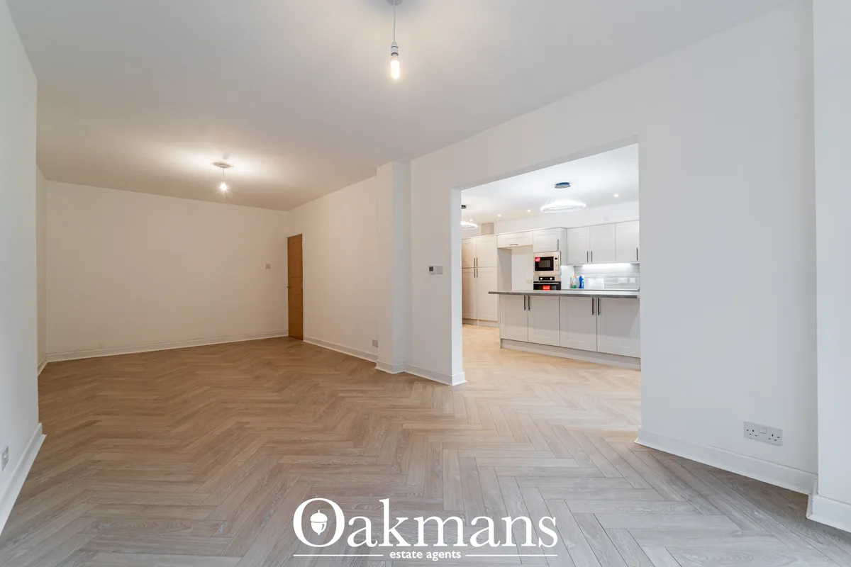 Bright open-plan living room with herringbone wood flooring, white walls, pendant lighting and open access to fitted kit