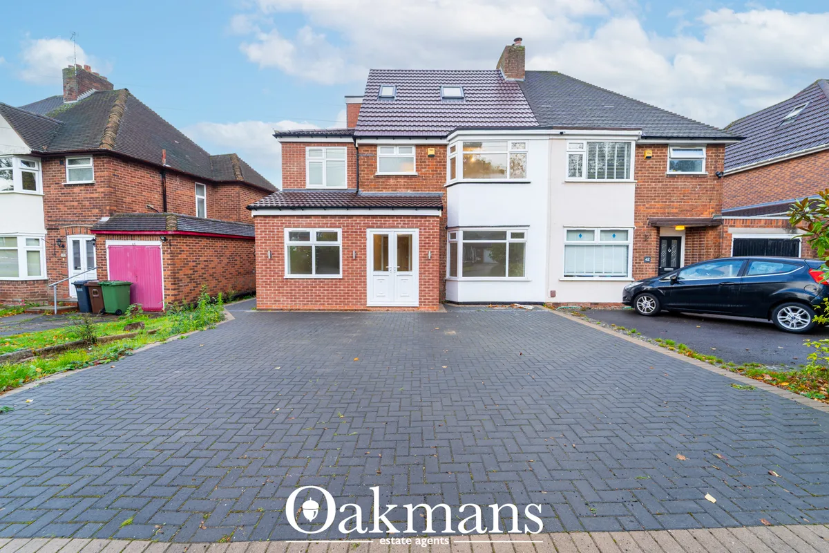 Red brick semi-detached house with white rendered upper storey, dark roof tiles, paved driveway, parked car and neighbou