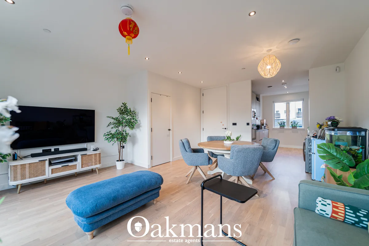 Open-plan living room with blue upholstered furniture, wooden dining table, wall-mounted TV, recessed lighting and conte