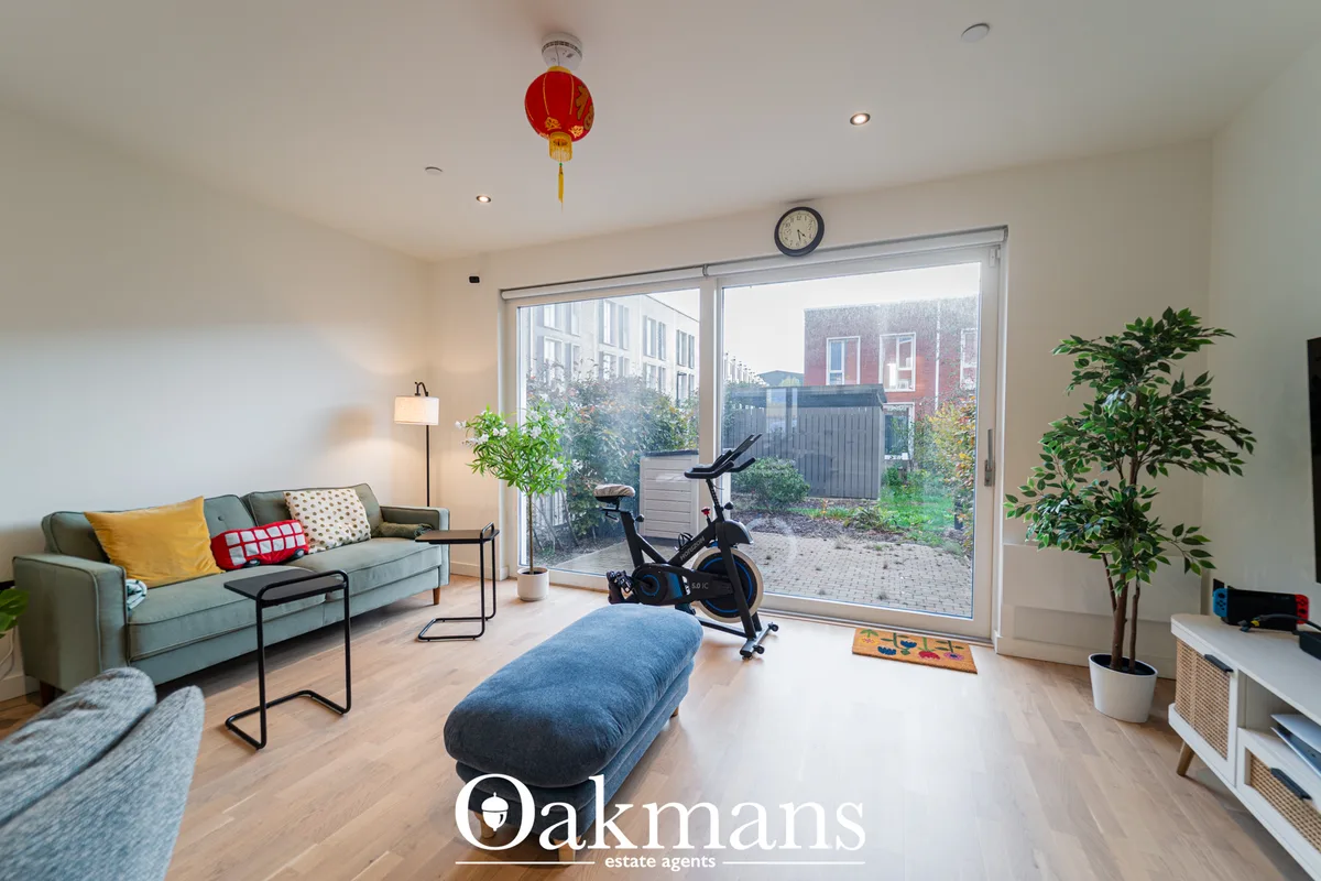 Bright living room with sage green sofa, exercise bike, blue storage bench, large sliding glass doors opening to garden 