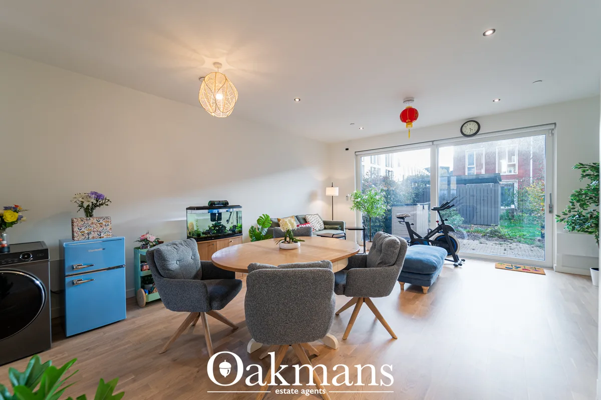 Open-plan living space with round wooden dining table, grey upholstered chairs, blue retro fridge, aquarium, exercise bi